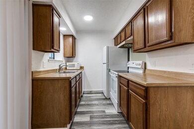 Kitchen with white appliances, dark wood-style flooring, light countertops, and brown cabinetry