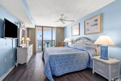 Bedroom with dark wood-style floors, expansive win