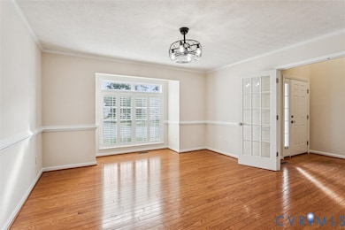 Unfurnished dining area featuring ornamental molding, light wood-type flooring, a textured ceiling, and a chandelier