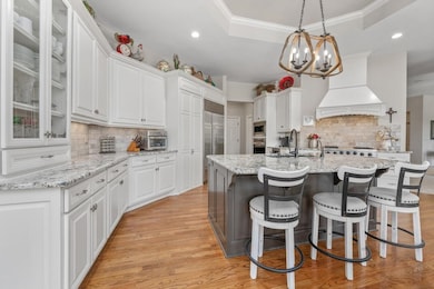 Kitchen featuring a raised ceiling, white cabinets, light stone counters, pendant lighting, and recessed lighting