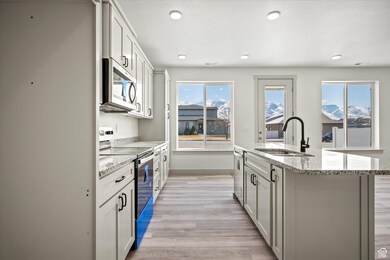 Kitchen featuring light stone countertops, an island with sink, a sink, light wood-style floors, and appliances with stainless steel finishes
