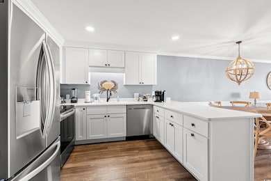 Kitchen with appliances with stainless steel finishes, a peninsula, ornamental molding, light countertops, and white cabinets