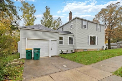 View of side of property with a lawn, roof with shingles, concrete driveway, an attached garage, and a chimney