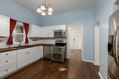 Kitchen featuring stainless steel appliances, white cabinetry, pendant lighting, dark wood-style floors, and tasteful backsplash