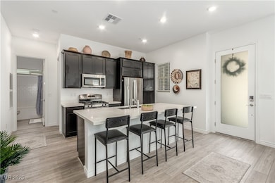 Kitchen with a breakfast bar, a center island with sink, appliances with stainless steel finishes, light countertops, and light wood-type flooring