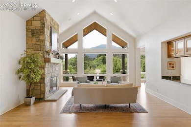 Living room with a stone fireplace, healthy amount of natural light, wood finished floors, and high vaulted ceiling