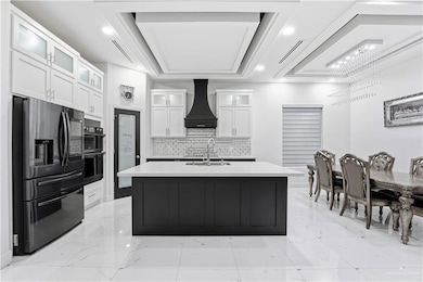 Kitchen featuring glass insert cabinets, stainless steel fridge with ice dispenser, white cabinetry, backsplash, and custom exhaust hood