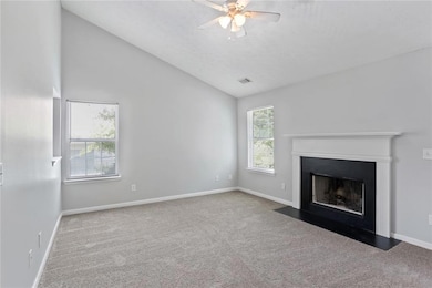 Unfurnished living room featuring carpet flooring, plenty of natural light, a ceiling fan, and vaulted ceiling