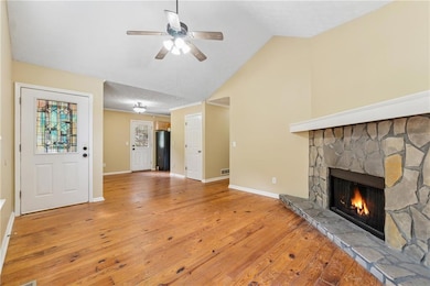Unfurnished living room with a stone fireplace, wood-type flooring, a ceiling fan, and vaulted ceiling