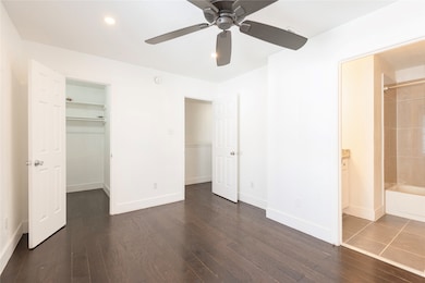 Unfurnished bedroom with a walk in closet, connected bathroom, dark wood finished floors, recessed lighting, and ceiling fan