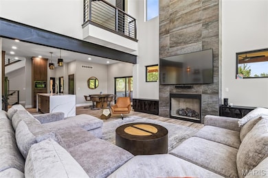 Living room with a towering ceiling, light wood finished floors, a tile fireplace, recessed lighting, and stairway