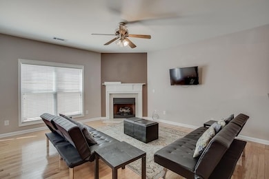 Living room with ceiling fan, light wood-type flooring, and a fireplace with raised hearth