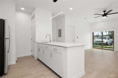 Kitchen with stainless steel refrigerator, light wood-type flooring, ceiling fan, hanging light fixtures, and sink