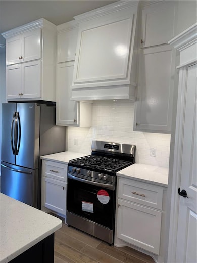Kitchen with stainless steel stove, backsplash, fridge, white cabinetry, and light stone countertops