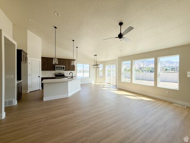 Unfurnished living room featuring a textured ceiling, light wood-type flooring, lofted ceiling, and ceiling fan
