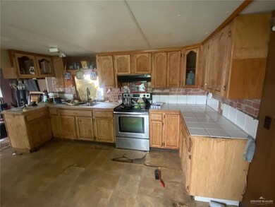 Kitchen featuring stainless steel electric range, tile counters, under cabinet range hood, backsplash, and glass insert cabinets