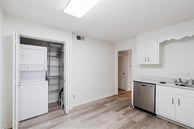 Kitchen with stacked washer / dryer, sink, light hardwood / wood-style flooring, and stainless steel dishwasher