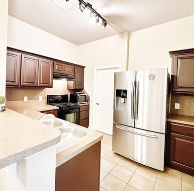 Kitchen featuring stainless steel appliances, track lighting, under cabinet range hood, and light tile patterned floors