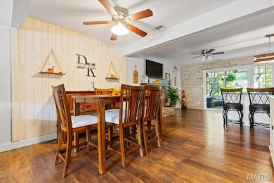 Dining area featuring dark wood-type flooring, wood walls, ceiling fan, and beamed ceiling