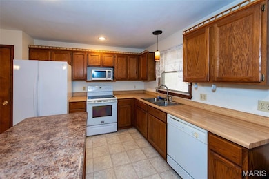 Kitchen with white appliances, pendant lighting, brown cabinetry, and light countertops