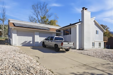 View of side of property featuring brick siding, driveway, a chimney, solar panels, and a garage