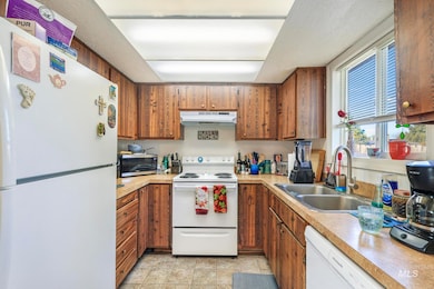Kitchen featuring white appliances, light countertops, under cabinet range hood, brown cabinetry, and light tile patterned floors