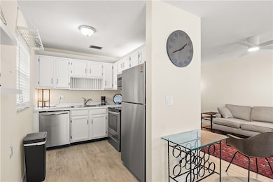 Kitchen with light wood-style flooring, appliances with stainless steel finishes, white cabinetry, light countertops, and open floor plan