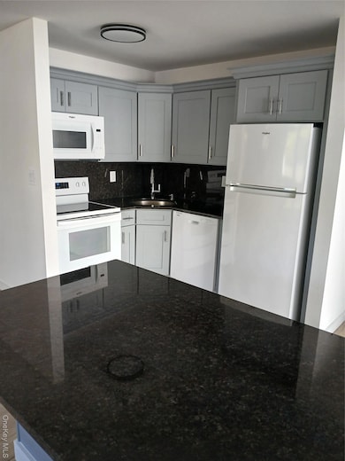 Kitchen featuring dark stone countertops, black refrigerator, range, and white microwave