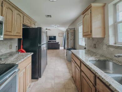 Kitchen featuring light tile flooring, tasteful backsplash, black fridge, and light stone countertops