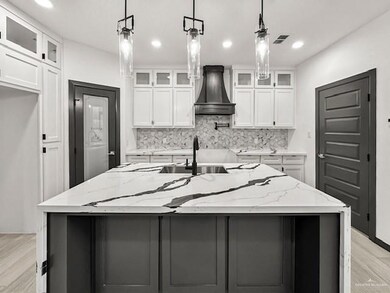 Kitchen with backsplash, custom range hood, an island with sink, white cabinetry, and light stone counters