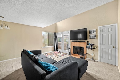 Carpeted living room featuring a tiled fireplace, a textured ceiling, and a textured wall