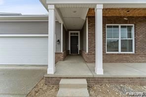 View of exterior entry featuring brick siding, a porch, and an attached garage