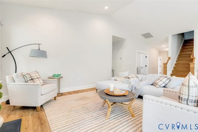 Living area with light wood-type flooring, vaulted ceiling, recessed lighting, and stairway
