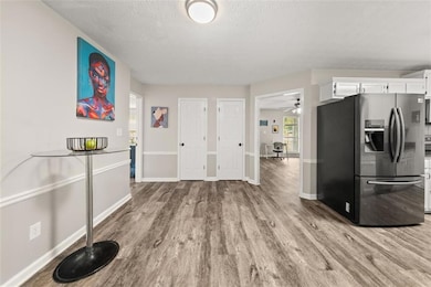 Kitchen featuring stainless steel refrigerator with ice dispenser, wood finished floors, white cabinets, baseboards, and a textured ceiling