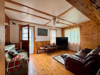 Living room with wooden walls, wood-type flooring, a wainscoted wall, and a ceiling fan