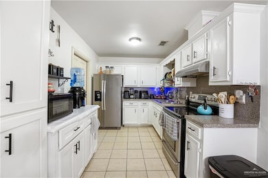 Kitchen featuring stainless steel appliances, under cabinet range hood, a sink, light tile patterned floors, and decorative backsplash