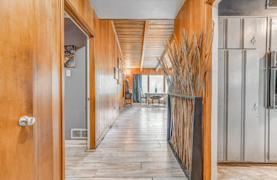 Hall with light wood-style flooring, wood walls, and wooden ceiling