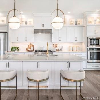 Kitchen featuring glass insert cabinets, a kitchen breakfast bar, white cabinetry, stainless steel appliances, and recessed lighting