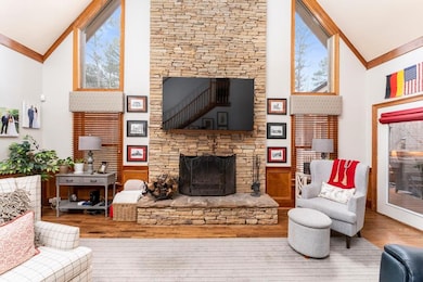 Living room with high vaulted ceiling, a stone fireplace, wood finished floors, crown molding, and plenty of natural light