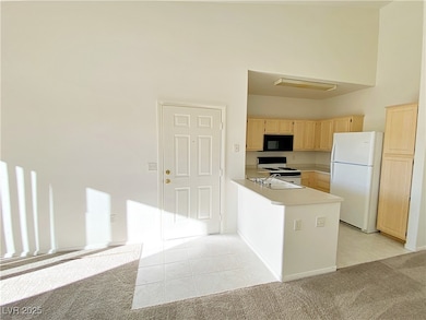 Kitchen with light brown cabinets, white appliances, light tile patterned floors, a peninsula, and light countertops