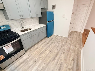 Kitchen with gray cabinetry, stainless steel range with gas stovetop, light wood-type flooring, tasteful backsplash, and light stone counters