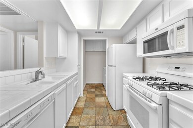 Kitchen with tile countertops, white appliances, and white cabinets