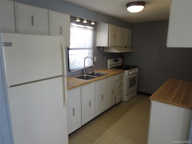 Kitchen with white appliances, butcher block countertops, light tile patterned flooring, ventilation hood, and white cabinetry