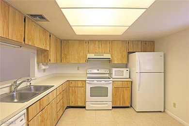 Kitchen featuring white appliances, light countertops, light tile patterned floors, and under cabinet range hood