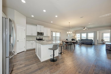 Kitchen with stainless steel appliances, open floor plan, decorative light fixtures, white cabinets, and an island with sink