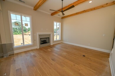 Unfurnished living room featuring beamed ceiling, a ceiling fan, light wood-type flooring, a tiled fireplace, and ornamental molding