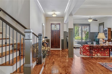 Entryway featuring ornamental molding, wood finished floors, ceiling fan, stairs, and a wainscoted wall