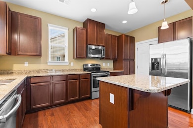 Kitchen featuring appliances with stainless steel finishes, a breakfast bar, dark hardwood / wood-style floors, decorative light fixtures, and a center island