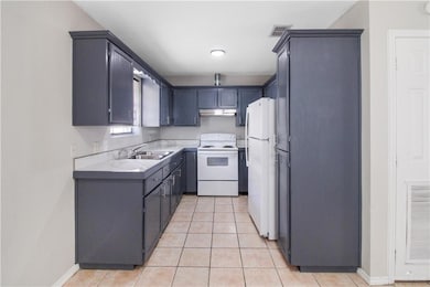 Kitchen featuring white appliances, light tile patterned floors, light countertops, under cabinet range hood, and gray cabinets