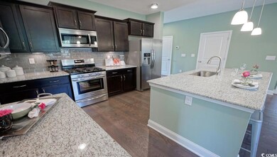 Kitchen featuring appliances with stainless steel finishes, a sink, dark wood-style floors, tasteful backsplash, and decorative light fixtures
